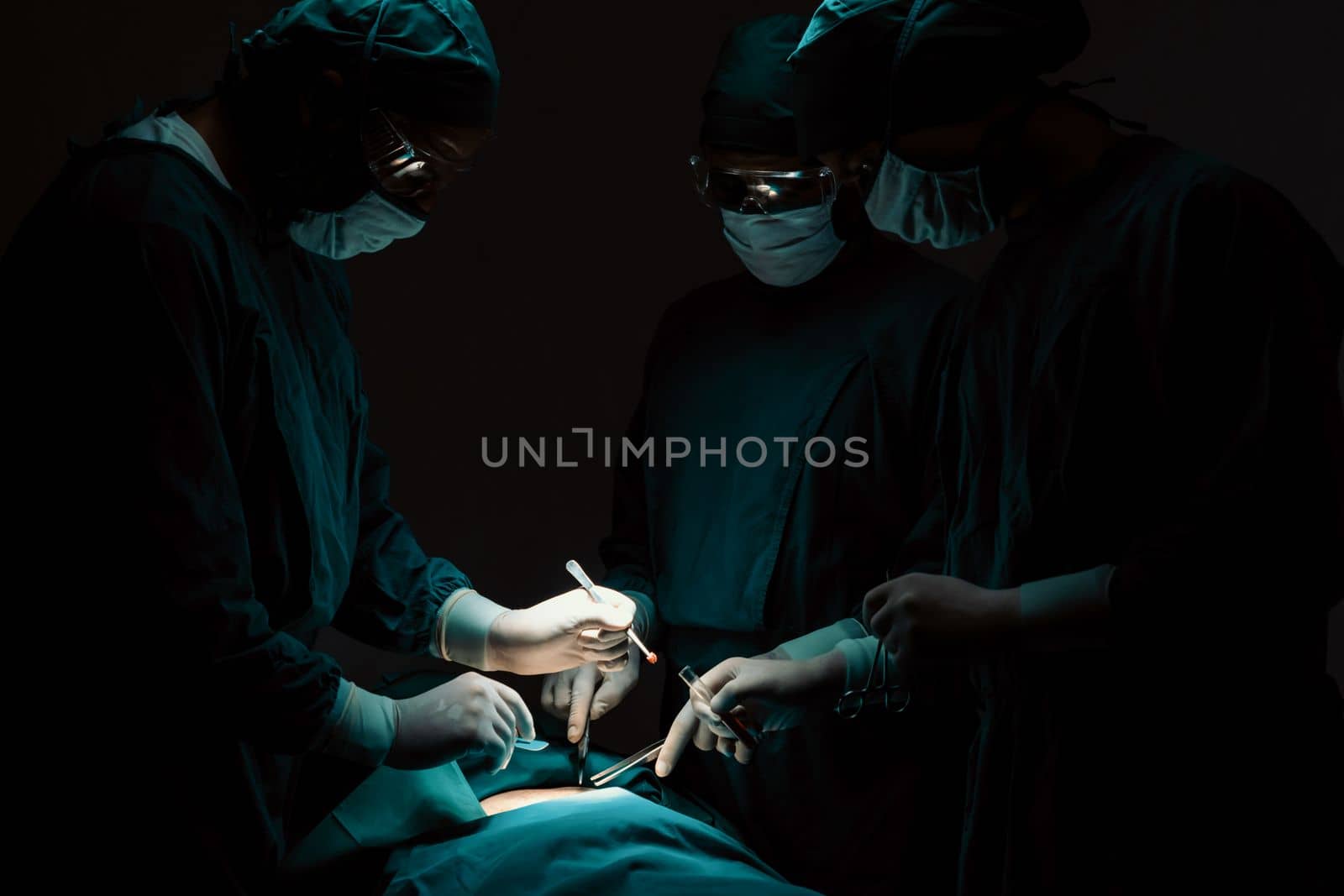 Surgical team performing surgery to patient in sterile operating room. In a surgery room lit by a lamp, a professional and confident surgical team provides medical care to an unconscious patient.