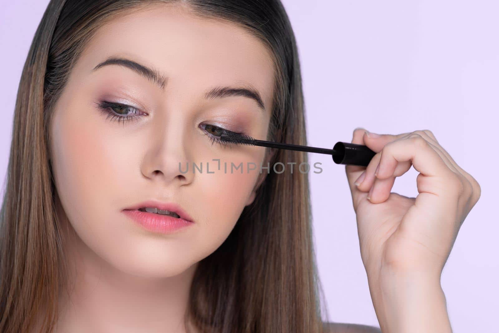 Closeup portrait of young charming applying makeup eyeshadow on her face with brush, mascara with flawless smooth skin for beauty concept.