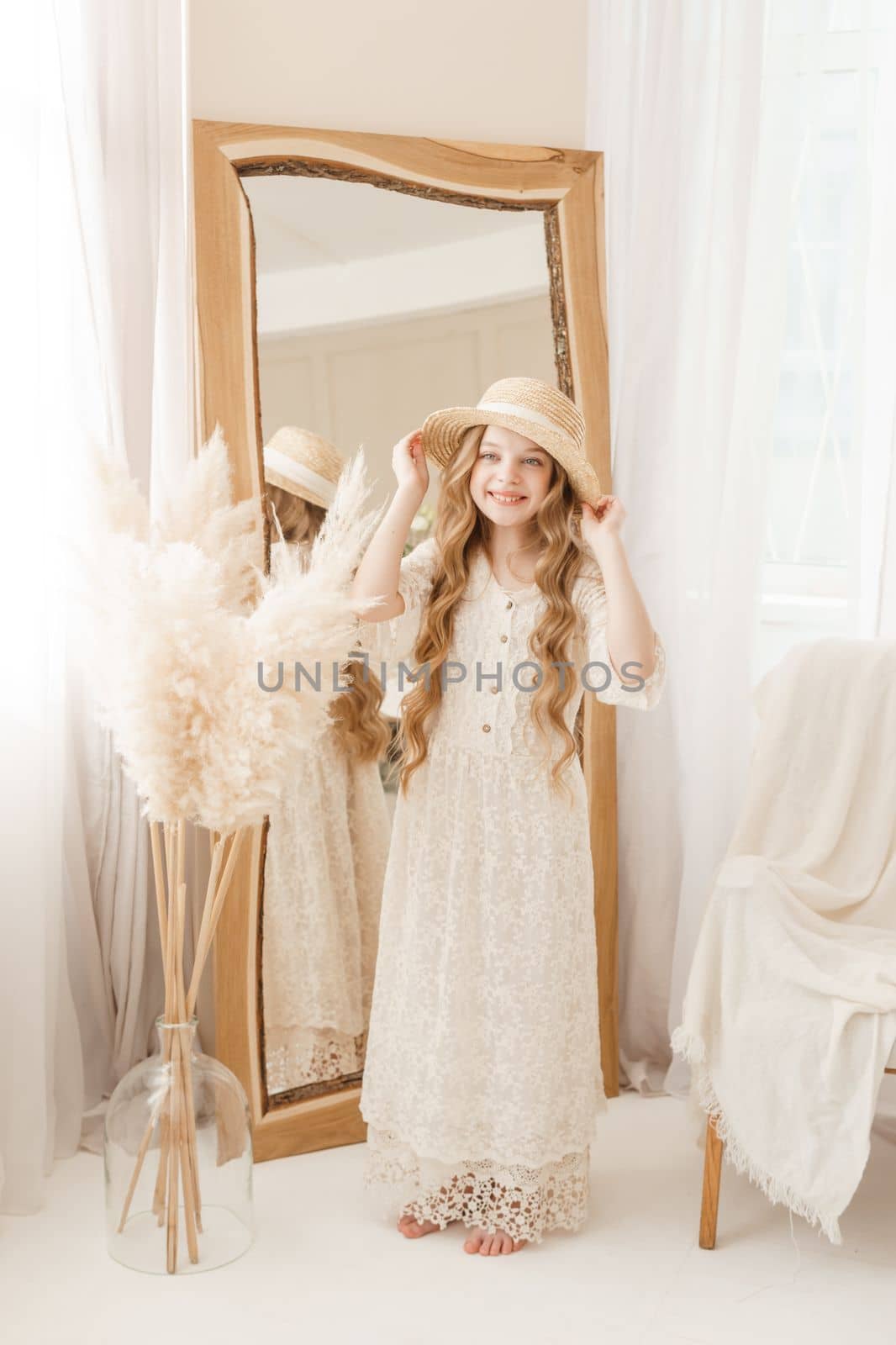 A beautiful teenage girl with long hair measures a straw hat in front of a mirror. Self-admiration of a blonde. selective focus
