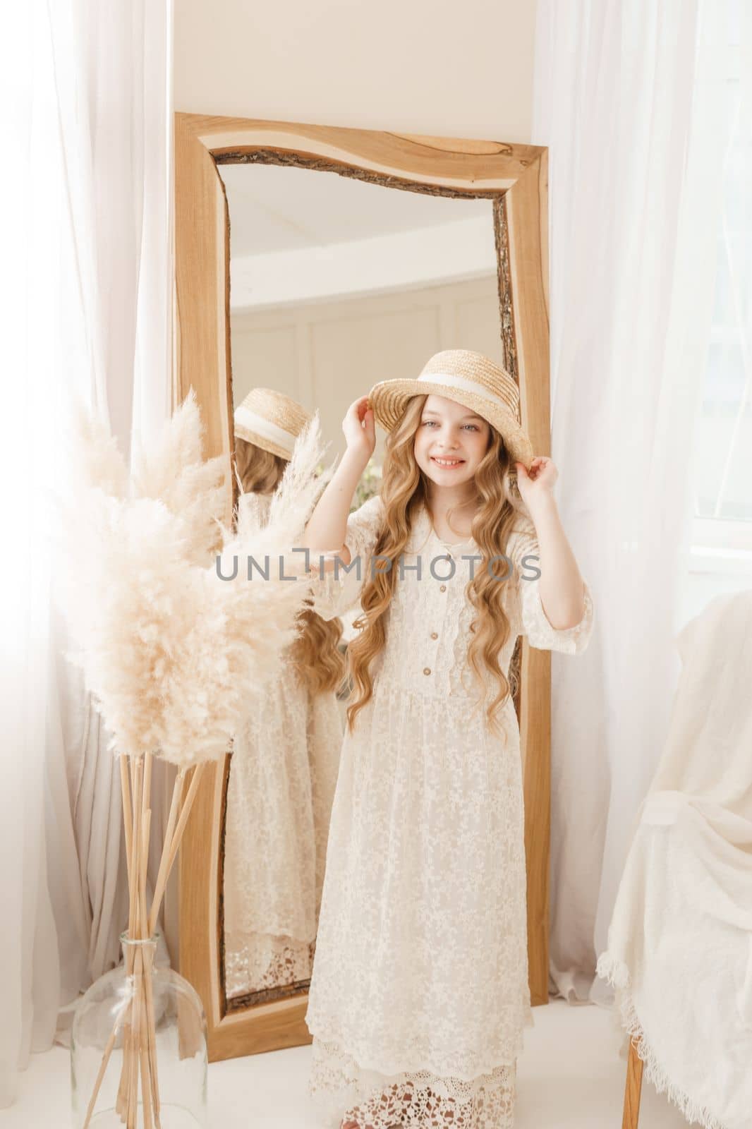 A beautiful teenage girl with long hair measures a straw hat in front of a mirror. Self-admiration of a blonde. selective focus