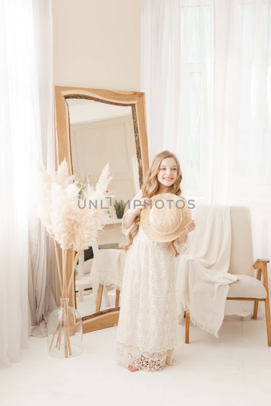 A beautiful teenage girl with long hair measures a straw hat in front of a mirror. Self-admiration of a blonde. selective focus