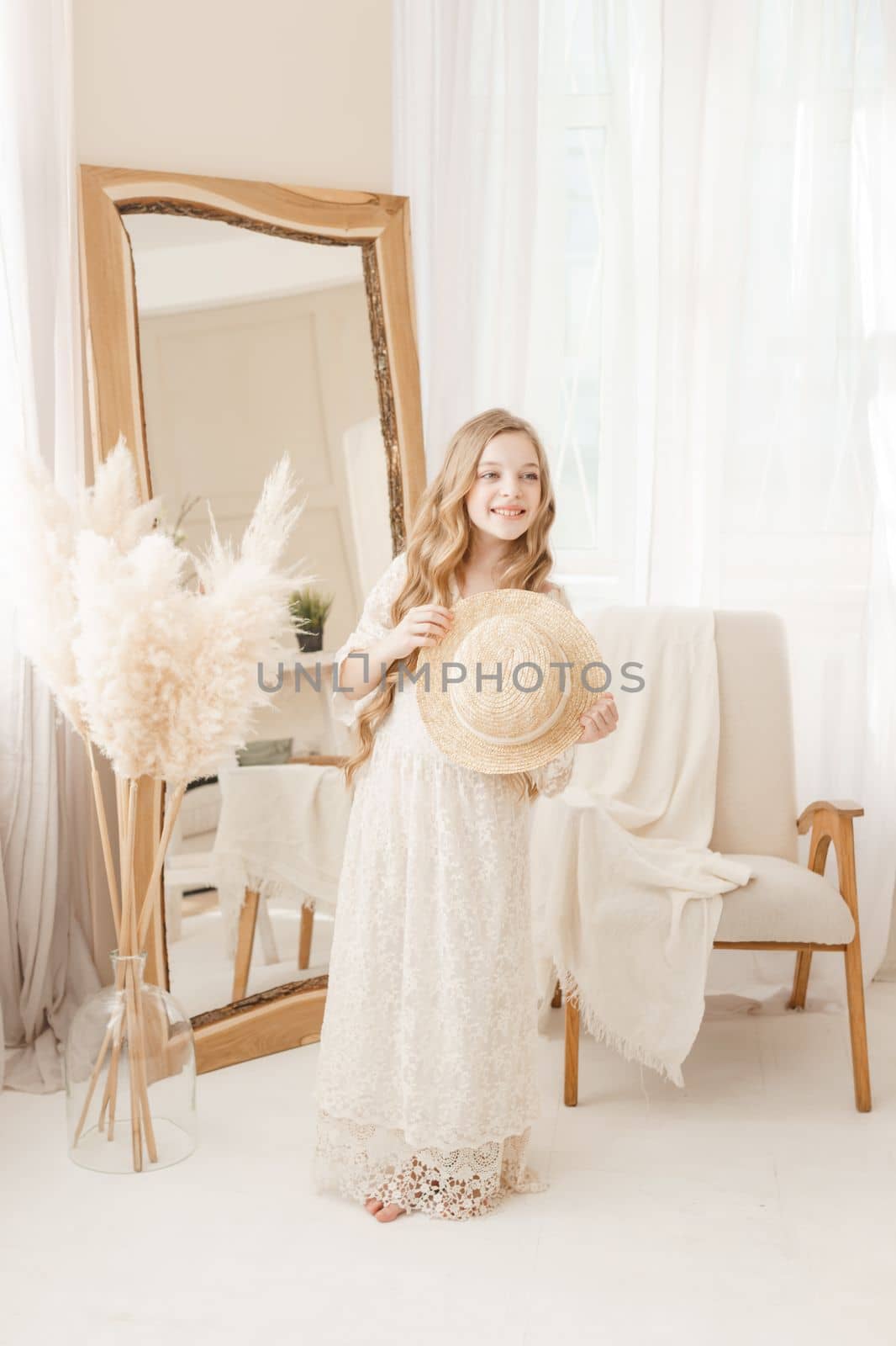A beautiful teenage girl with long hair measures a straw hat in front of a mirror. Self-admiration of a blonde. selective focus