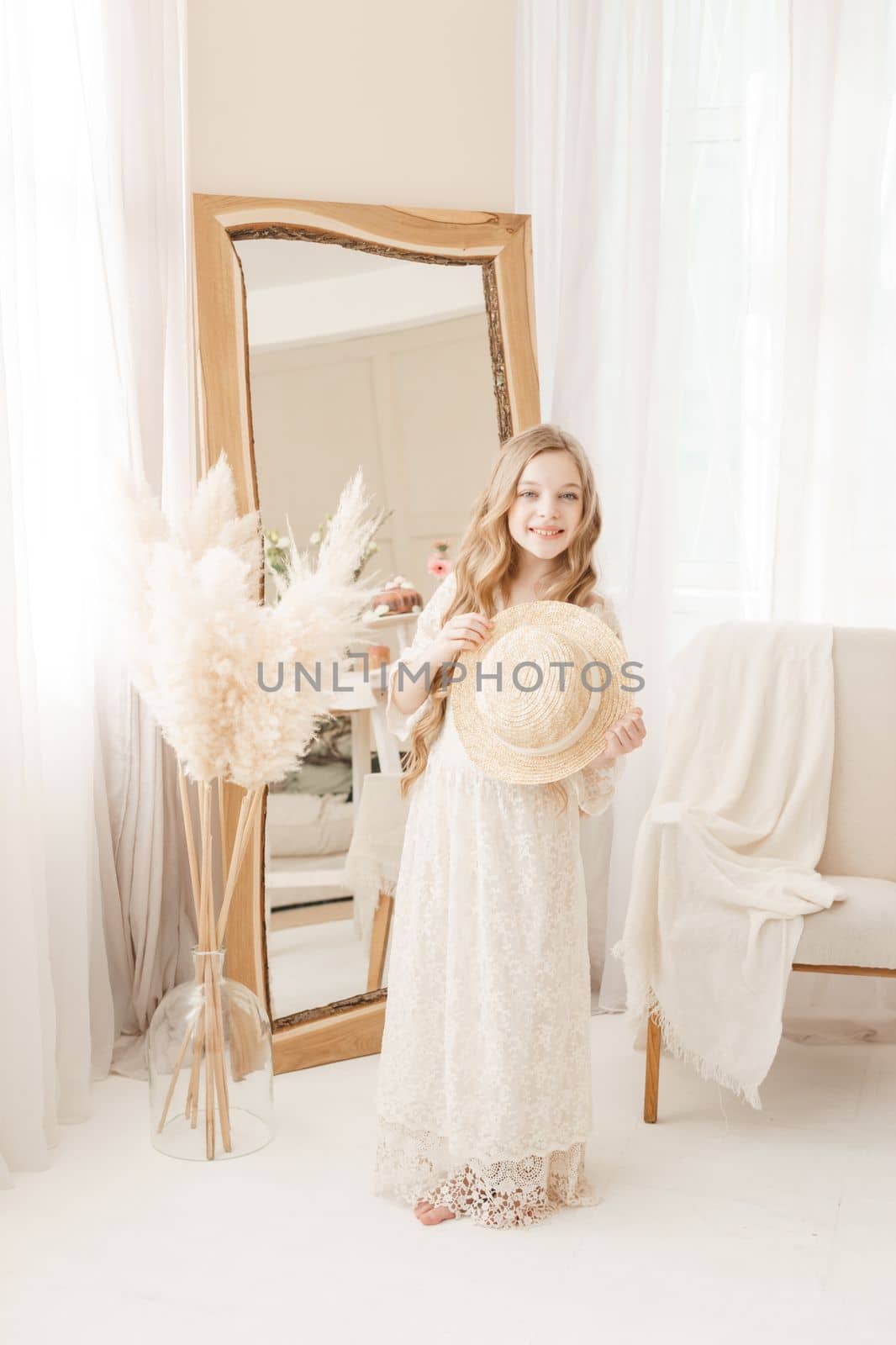A beautiful teenage girl with long hair measures a straw hat in front of a mirror. Self-admiration of a blonde. selective focus