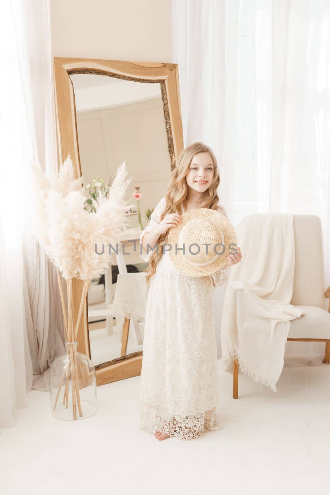 A beautiful teenage girl with long hair measures a straw hat in front of a mirror. Self-admiration of a blonde. selective focus