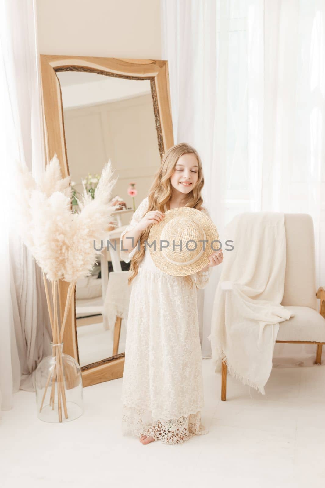 A beautiful teenage girl with long hair measures a straw hat in front of a mirror. Self-admiration of a blonde. selective focus