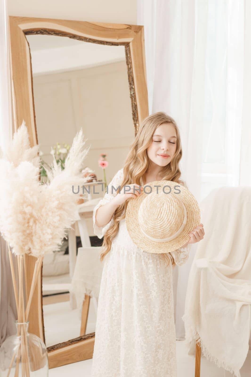 A beautiful teenage girl with long hair measures a straw hat in front of a mirror. Self-admiration of a blonde. selective focus