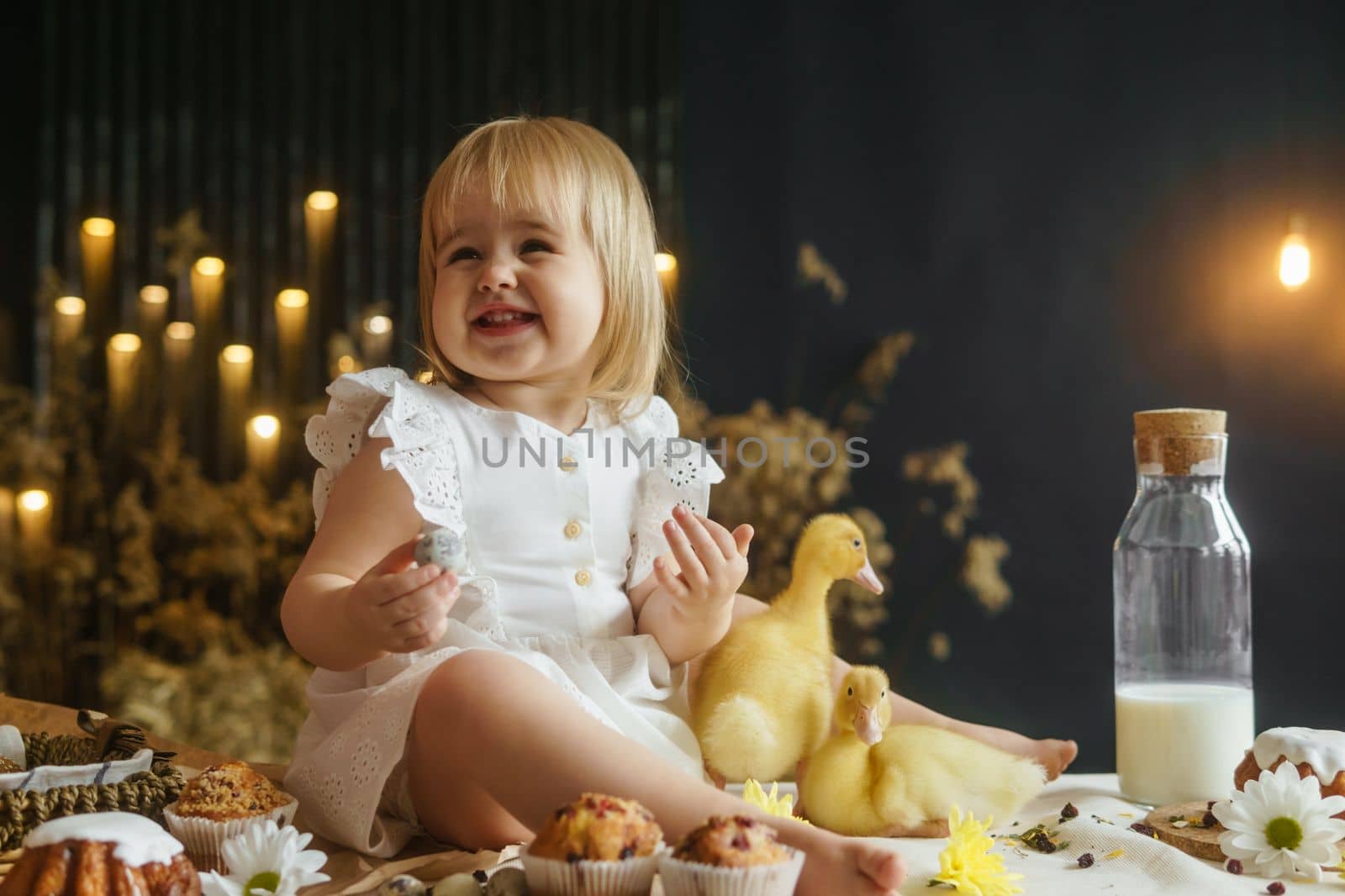 A little girl is sitting on the Easter table and playing with cute fluffy ducklings. The concept of celebrating happy Easter