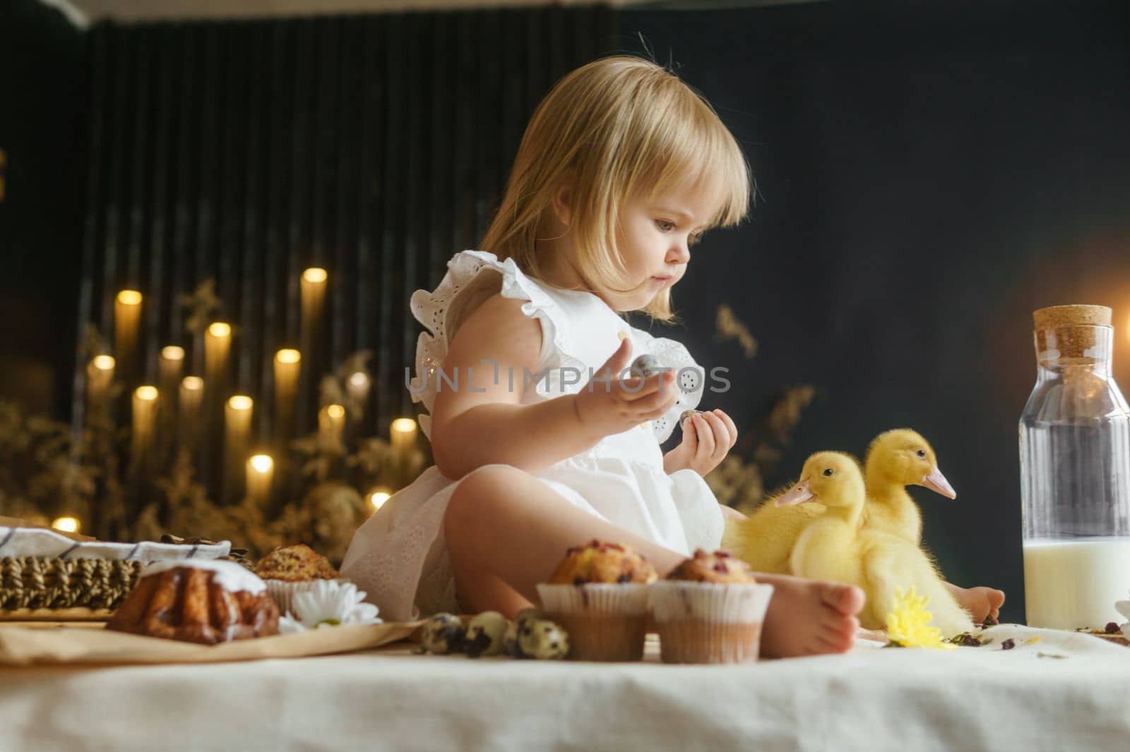 A little girl is sitting on the Easter table and playing with cute fluffy ducklings. The concept of celebrating happy Easter