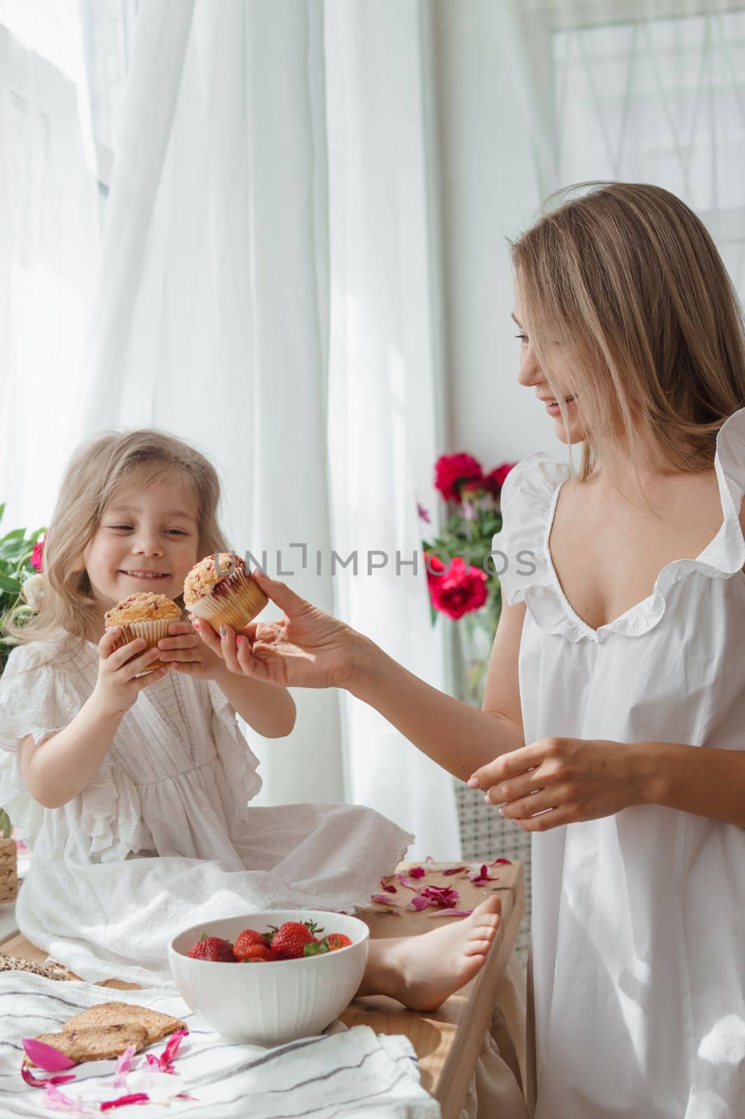 A little blonde girl with her mom on a kitchen countertop decorated with peonies. The concept of the relationship between mother and daughter. Spring atmosphere.