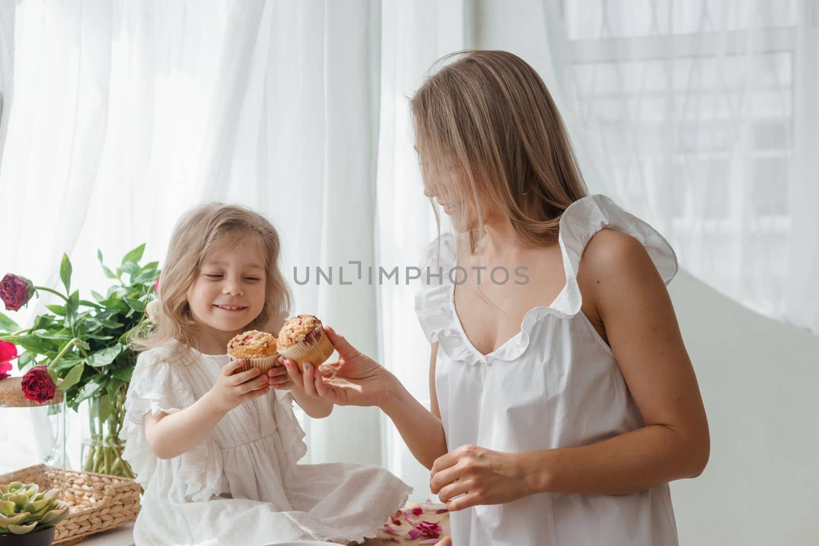 A little blonde girl with her mom on a kitchen countertop decorated with peonies. The concept of the relationship between mother and daughter. Spring atmosphere. by Annu1tochka