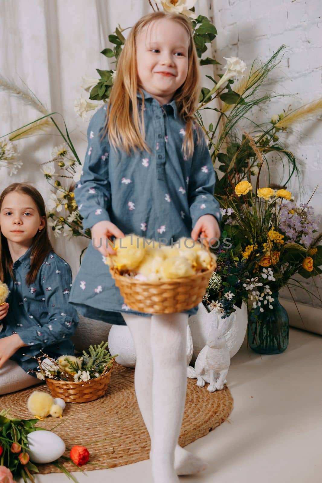 Two girls in a beautiful Easter photo zone with flowers, eggs, chickens and Easter bunnies. Happy Easter holiday