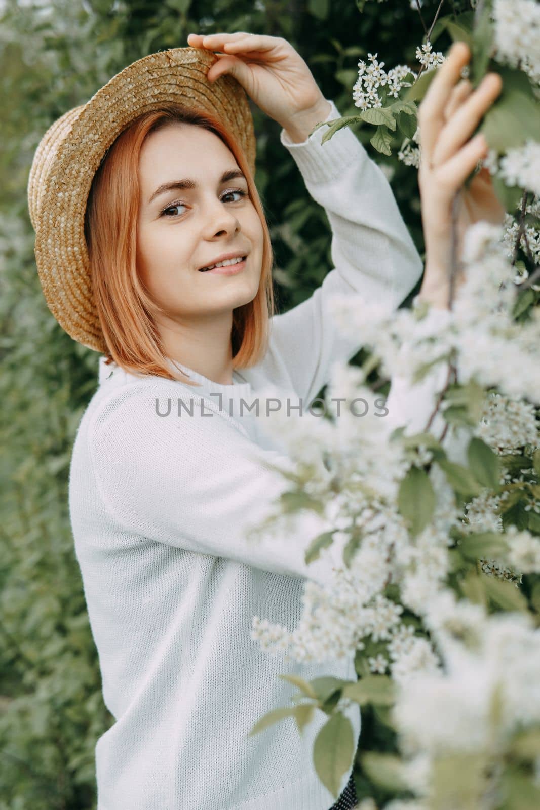 Portrait of a woman in a straw hat in a cherry blossom. Free outdoor recreation, spring blooming garden