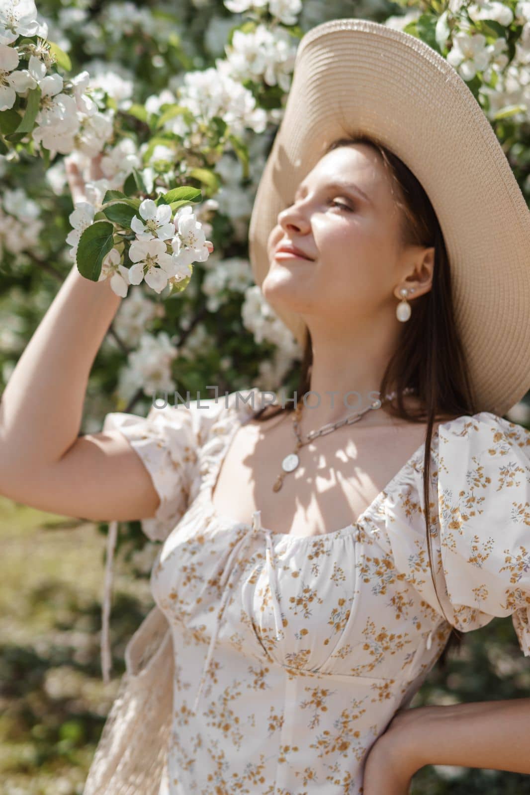 An attractive long-haired woman walks in the spring in the park of blooming apple trees. Spring portrait of a woman