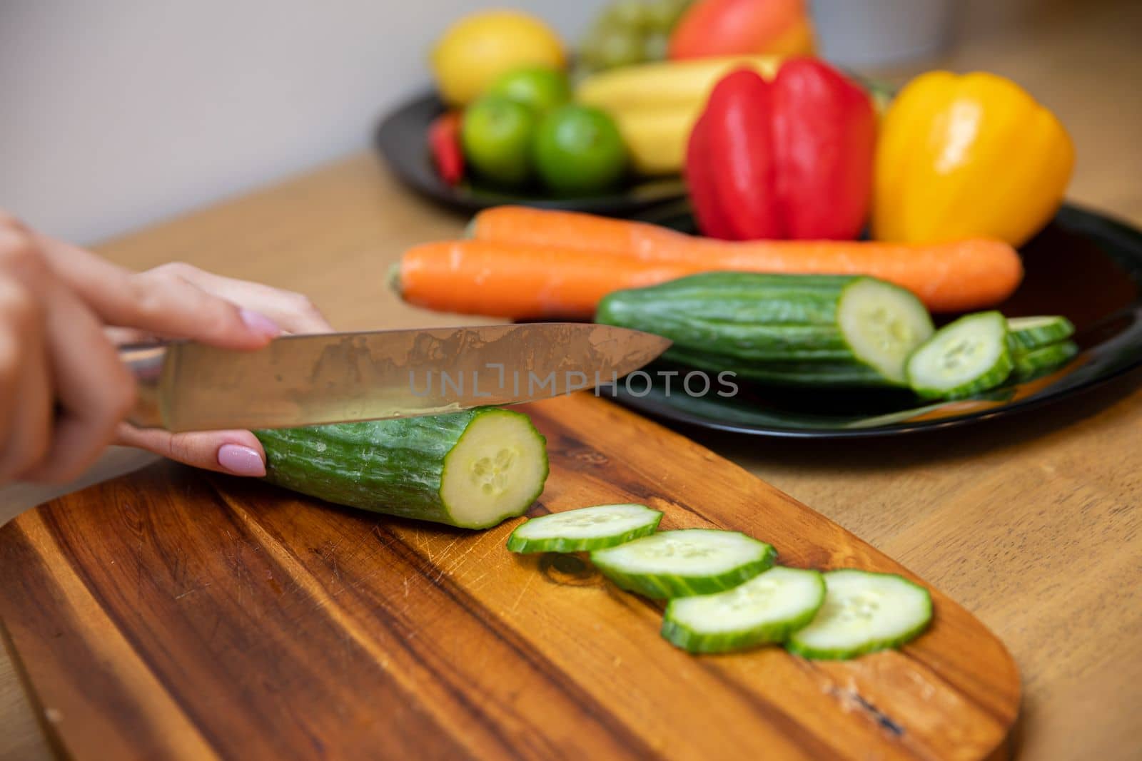 Autumn colored vegetables cut by a woman on a brown board. She slices peppers and carrots with a sharp knife.