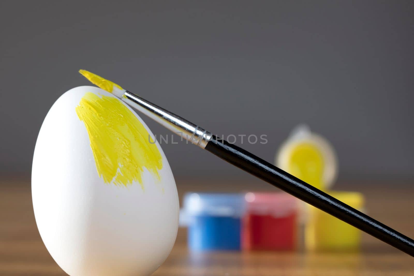 rough brush is painting a fragile easter egg with Yellow color, prepering for Holiday Happy Easter concept closeup colorful hobby