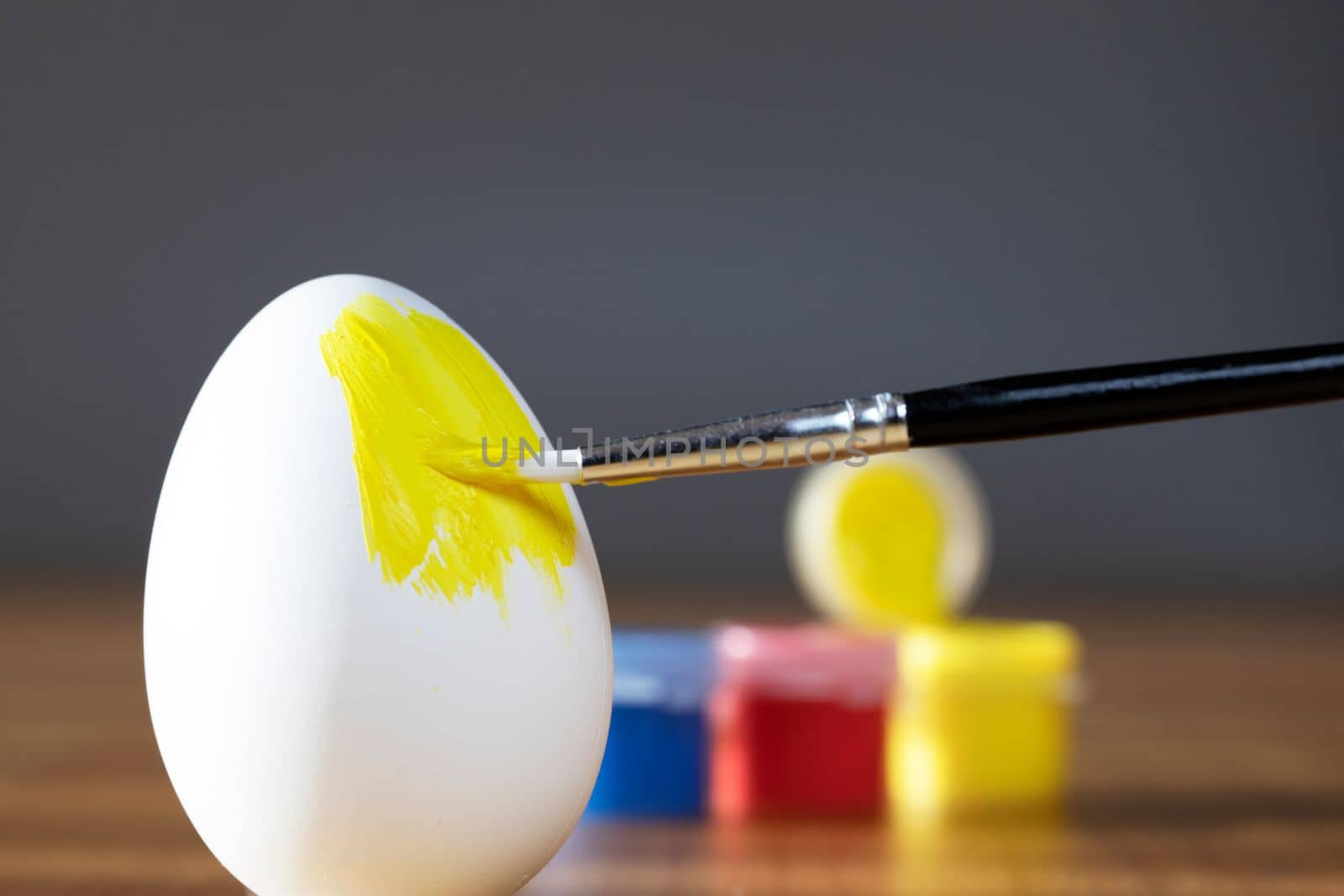 rough brush is painting a fragile easter egg with Yellow color, prepering for Holiday Happy Easter concept closeup colorful hobby