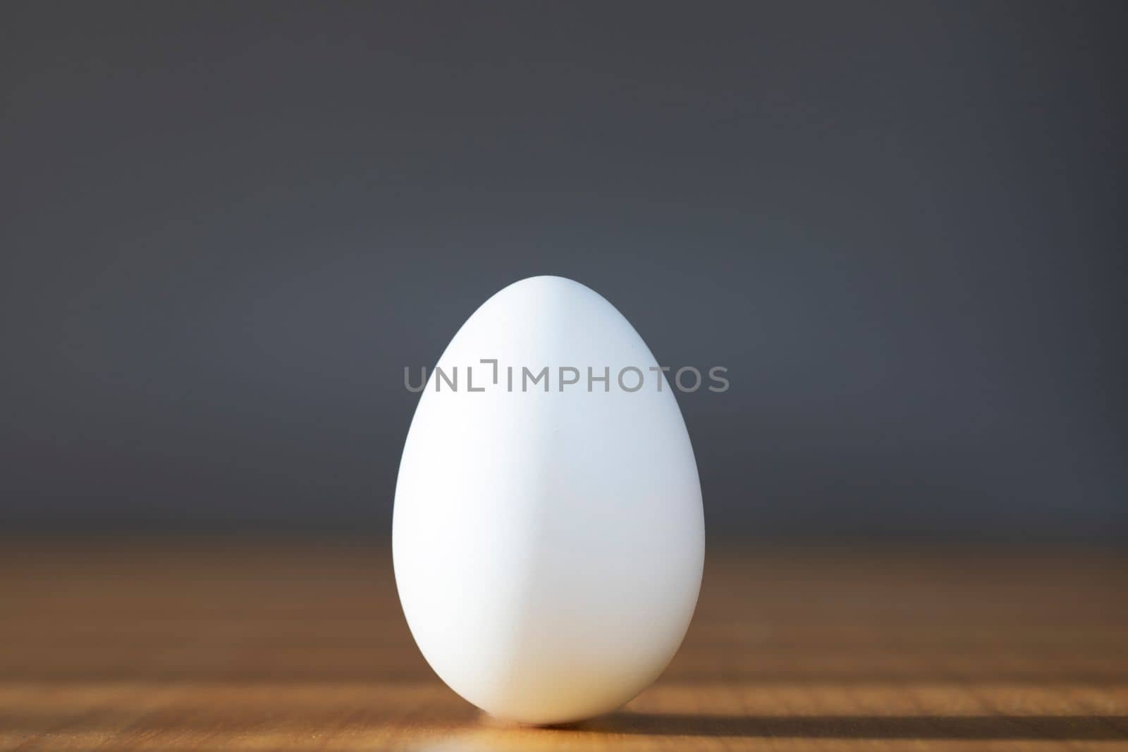 White egg on the gray background in center on wooden table . Design, visual art, minimalism food concept copy space