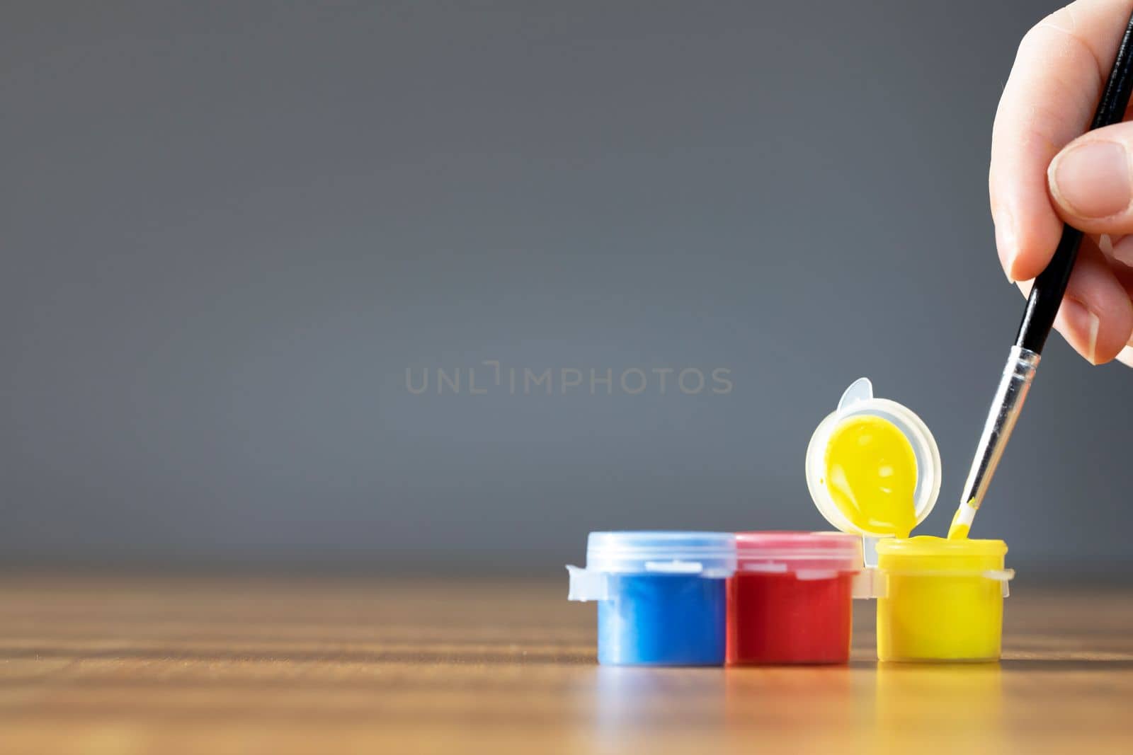 Artist paint brush with colorful paint on wooden table with gray background, copy space blue, red and yellow close up