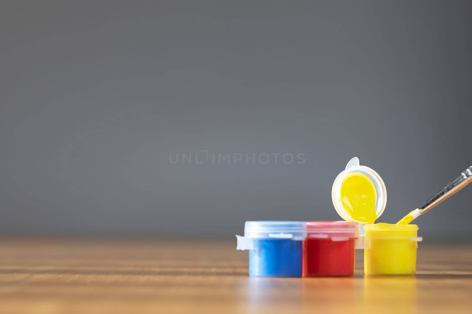 Artist paint brush with colorful paint on wooden table with gray background, copy space blue, red and yellow close up
