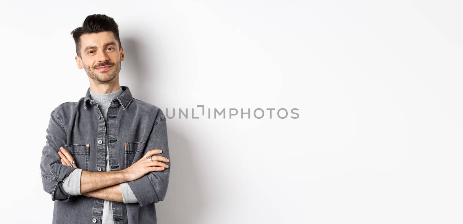 Proud handsome guy looking satisfied, cross arms on chest and smile at camera, checking out something good, standing on white background.