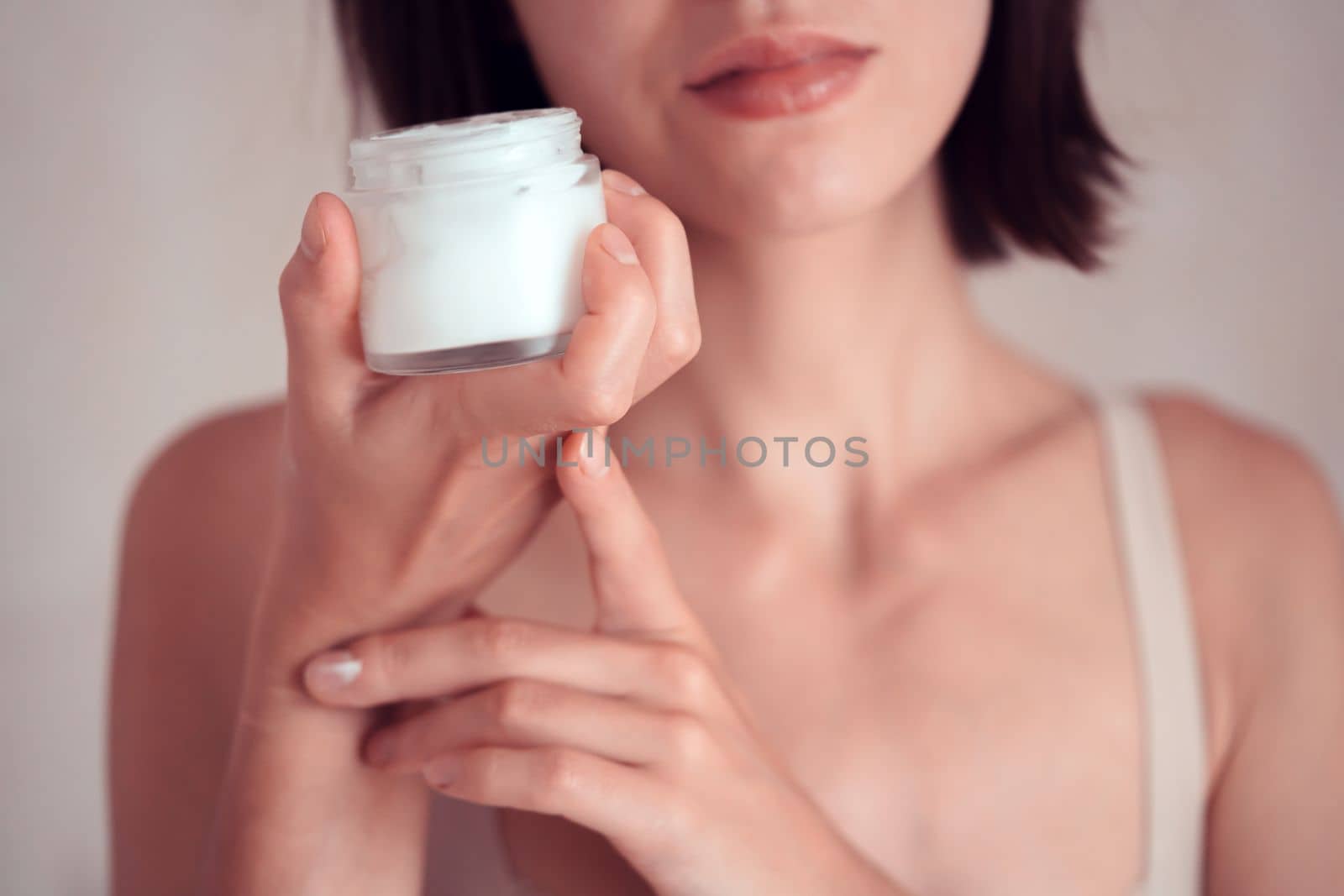 A young girl holds a jar of cream in her hands, applies a moisturizing balm to the body and face, takes care of beauty and health, close-up.