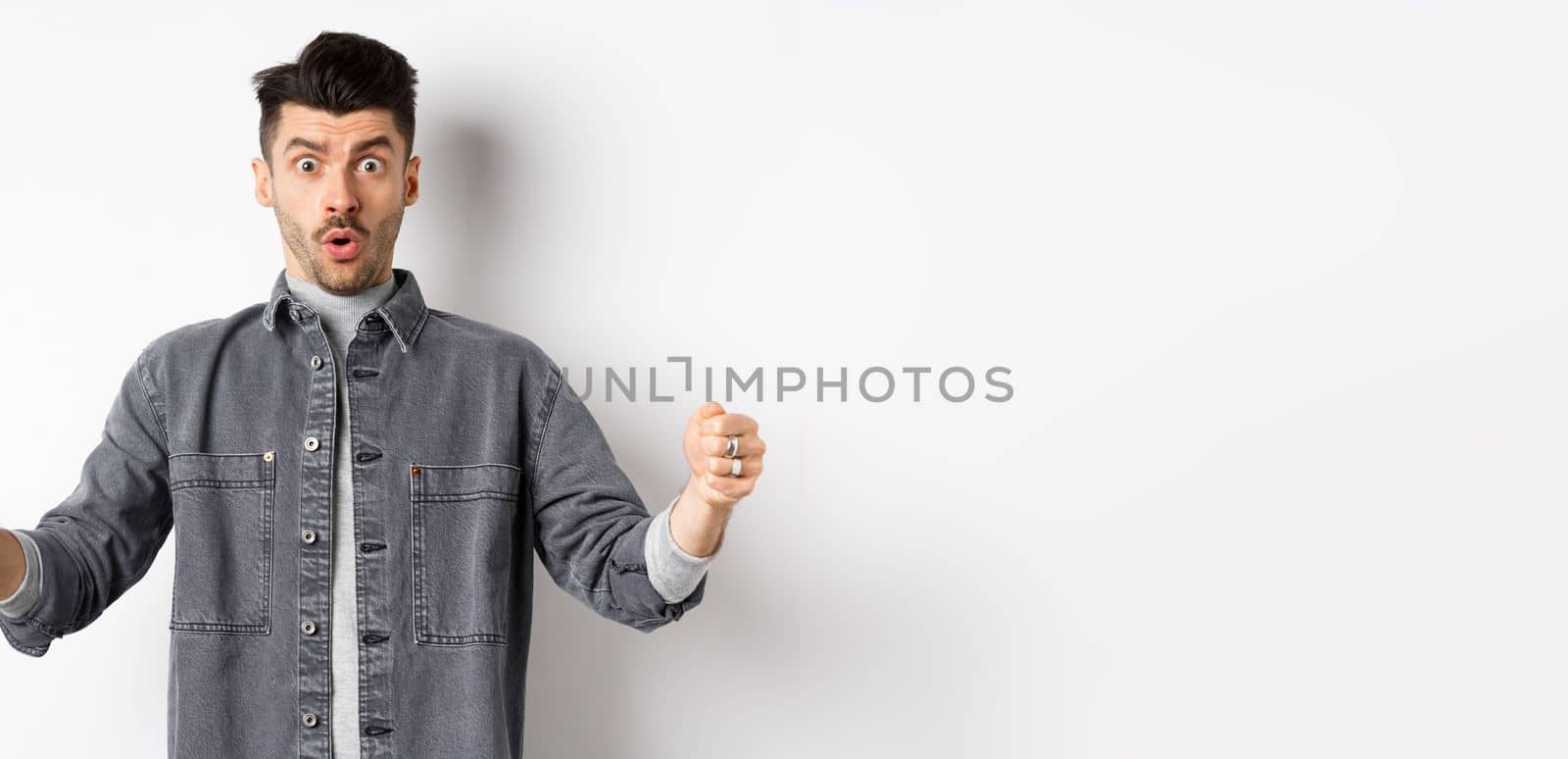 Confused man holding big size object and looking shocked, shaping large thing, standing on white background.