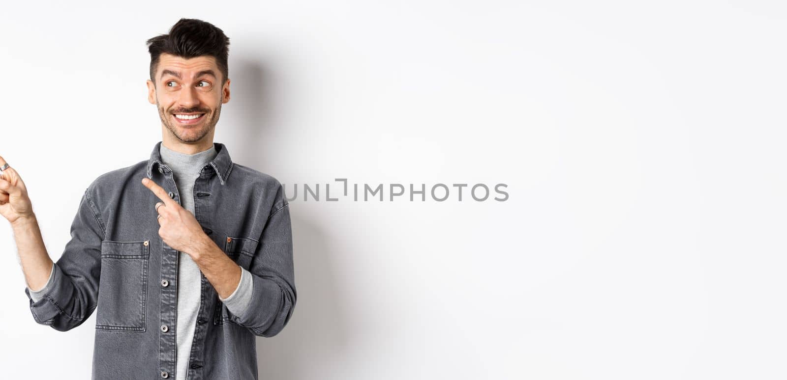 Happy handsome man smiling and pointing left at banner, showing cool product, standing on white background.