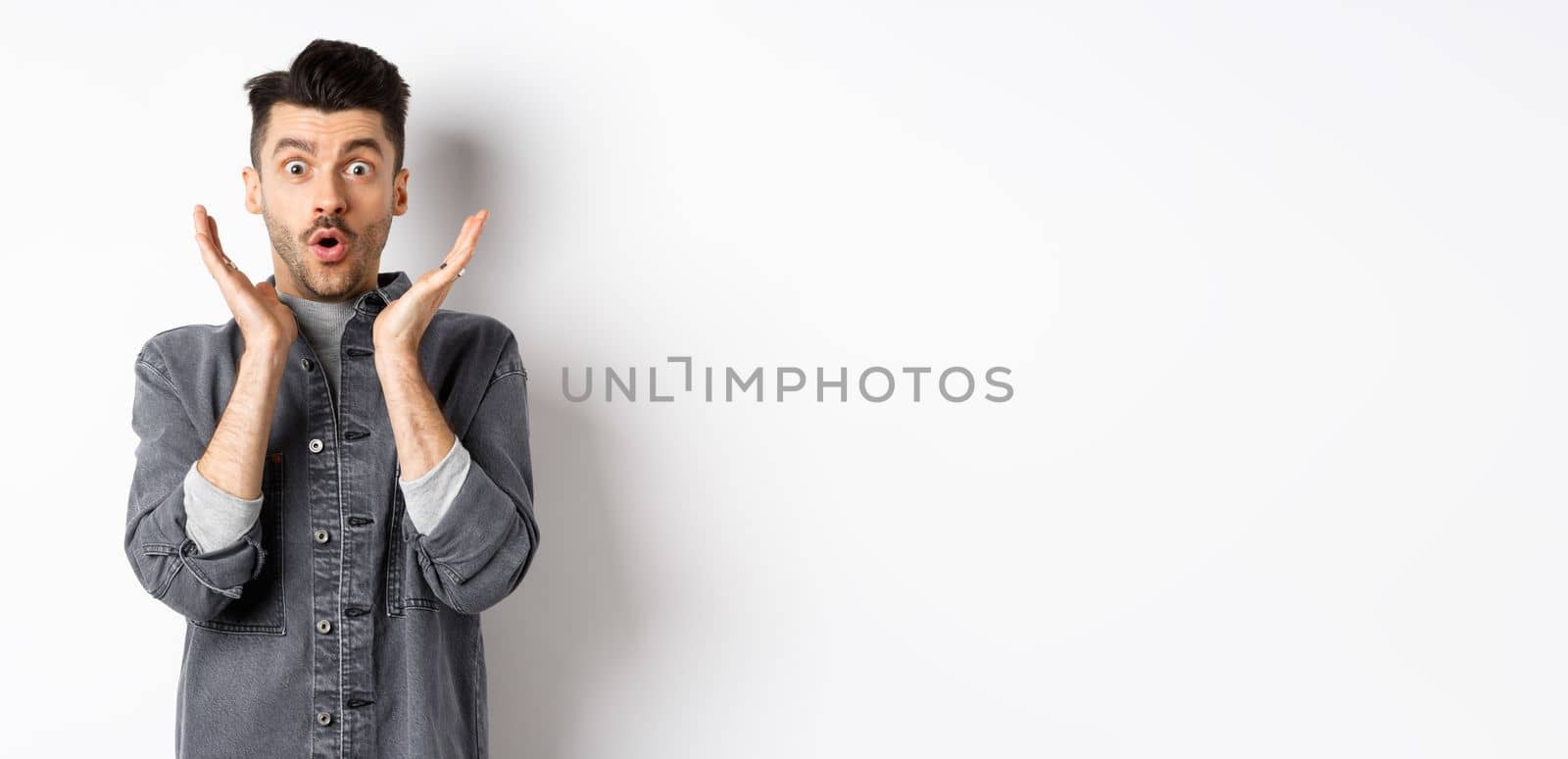 Surprised man gasping excited, say wow and look at amazing advertisement, standing on white background by Benzoix