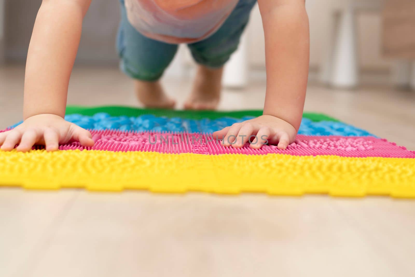 People. Health concept. A little boy stands in a plank on his arms and legs on a multi-colored orthopedic massage mat in a home interior. Close-up. blur. Soft focus. Rehabilitation.
