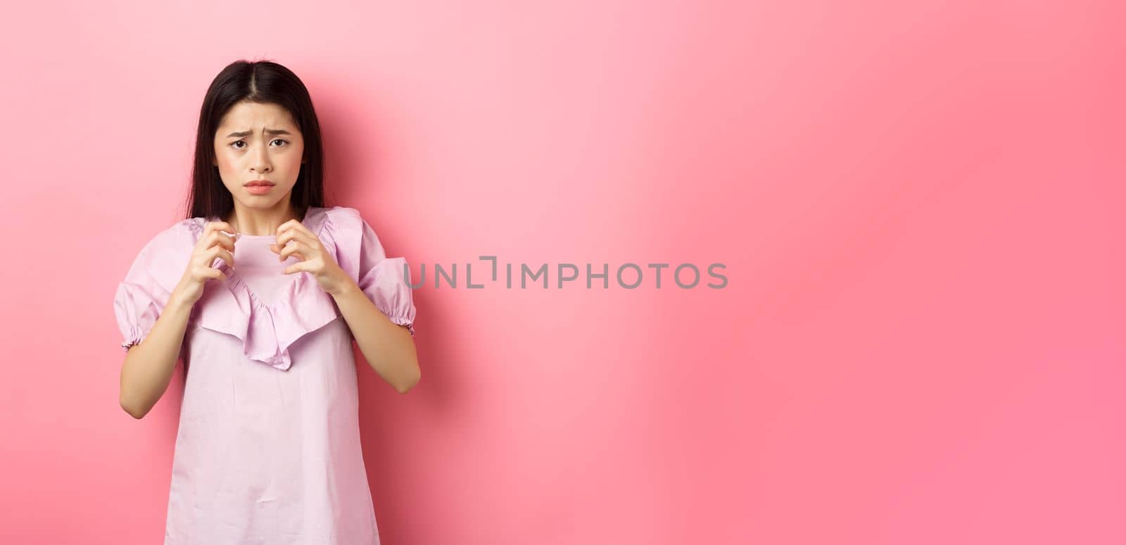 Scared asian woman victim, looking frightened, trembling from fear, stare at scary thing, standing anxious on pink background by Benzoix