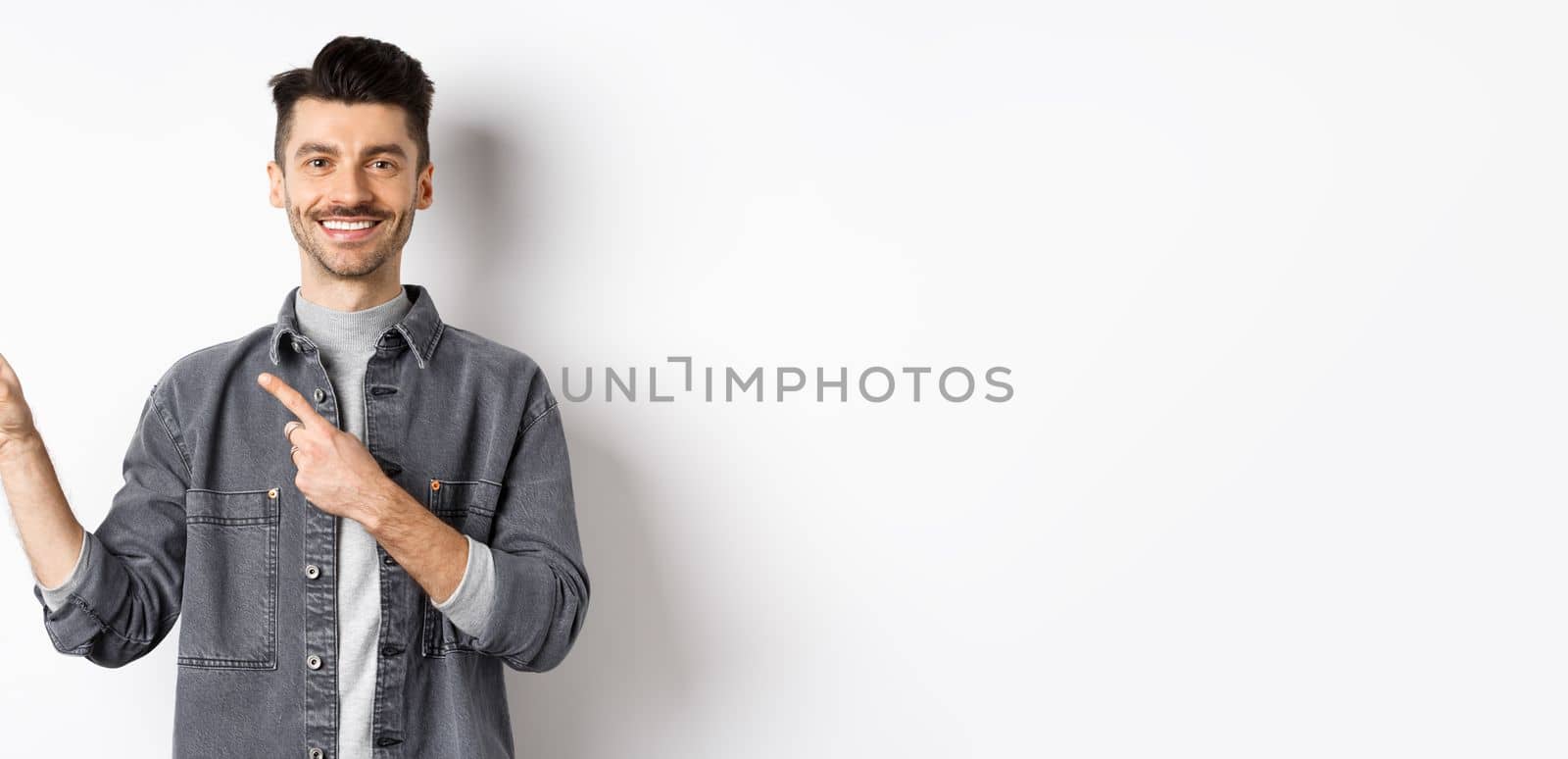 Handsome smiling man pointing fingers left, showing logo and looking cheerful at camera, advertising on white background by Benzoix