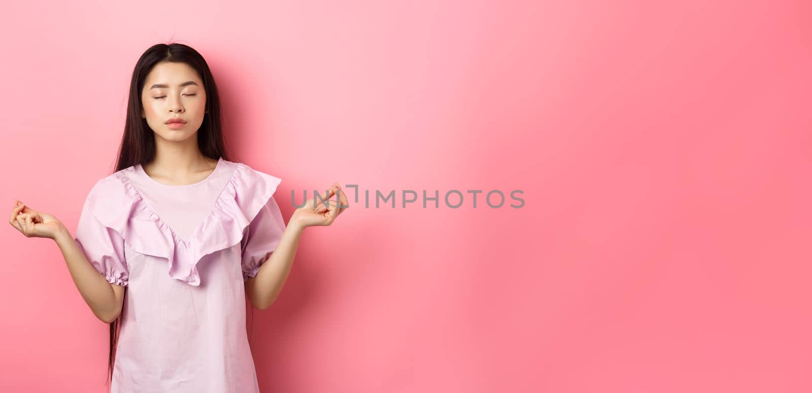 Stay calm. Peaceful asian woman meditating, hold hans in zen gseture and close eyes, practice yoga, standing patient on pink background.