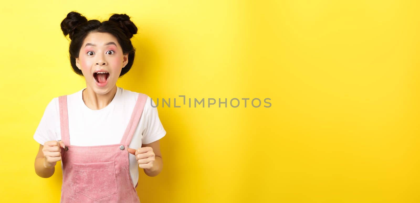 Excited asian woman open mouth, looking fascinated and amazed, receive good news, standing in summer clothes on yellow background by Benzoix