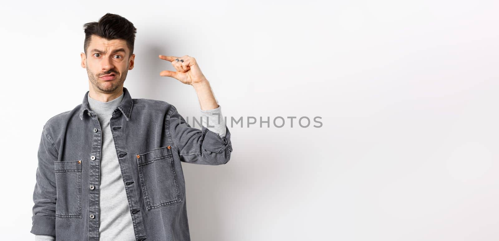 Disappointed guy showing small size and grimacing upset, frowning displeased with little thing, standing on white background.