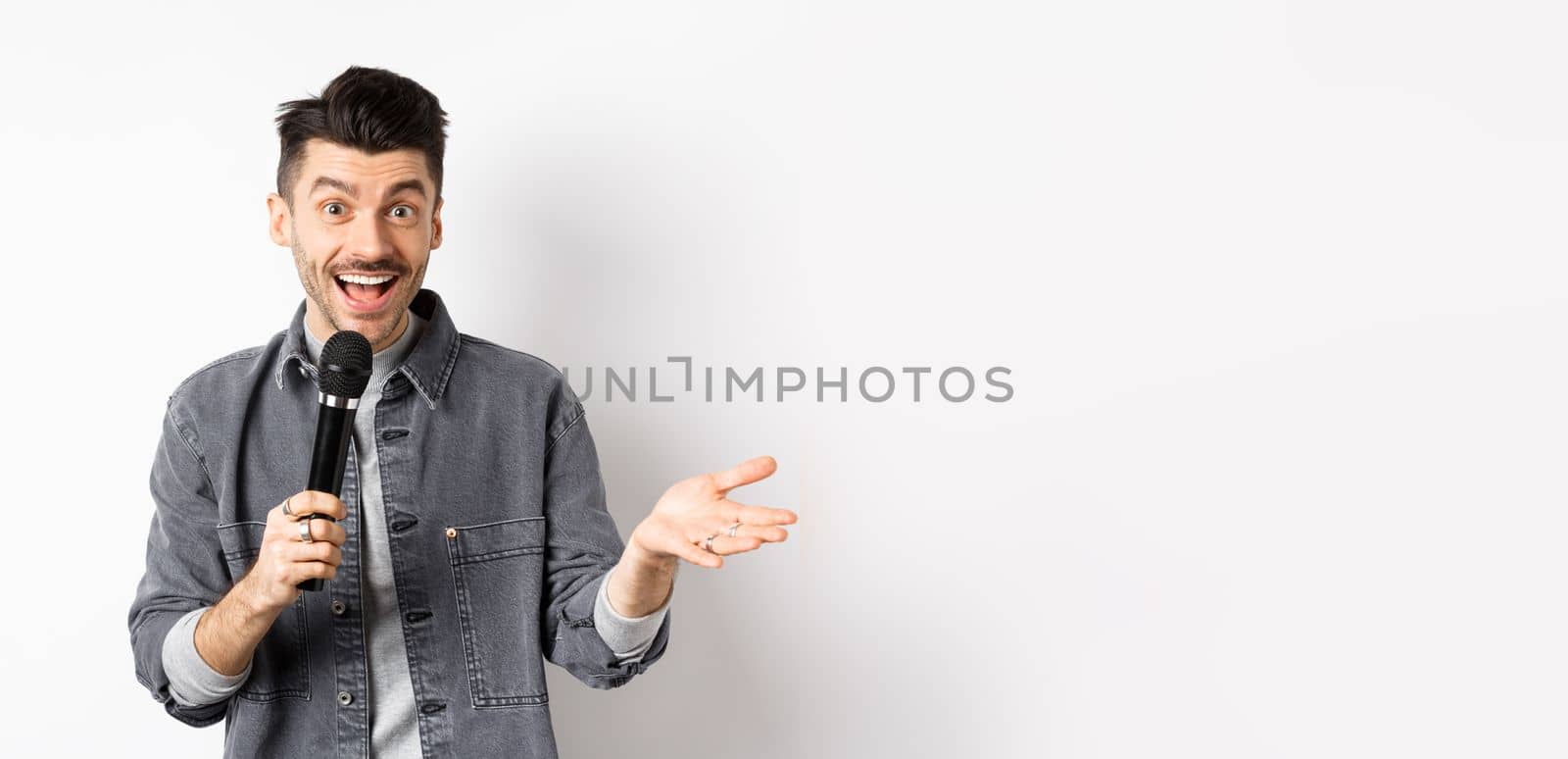 Handsome smiling performer talking in mic, gesturing and performing, making speech with microphone, standing against white background by Benzoix