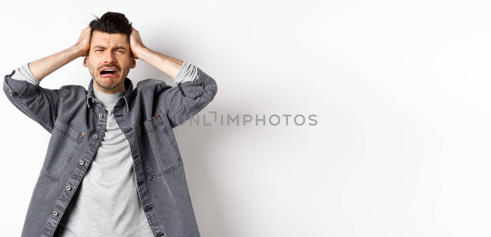 Frustrated guy crying and panicking, holding hands on head and screaming distressed, having trouble, standing upset on white background.