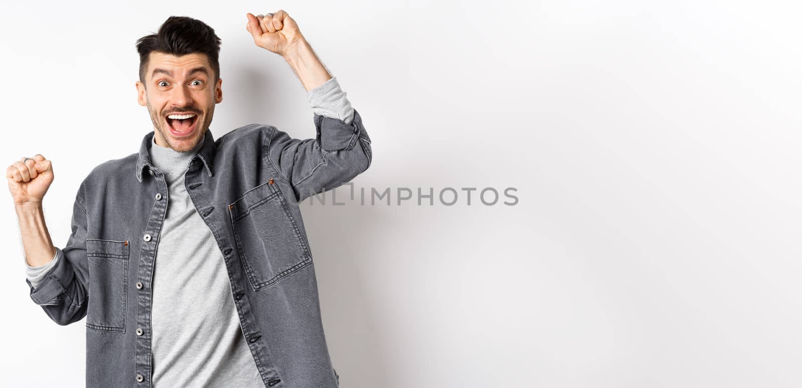 Excited man shouting from joy, winning prize and rejoicing, raising hands up and yelling yes with satisfied face, triumphing, achieve goal, standing on white background.