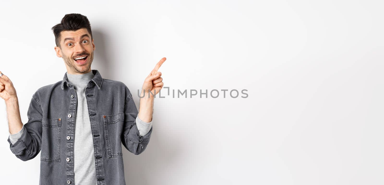Cheerful smiling man pointing fingers sideways, showing left and right ways, looking happy at camera, standing on white background.