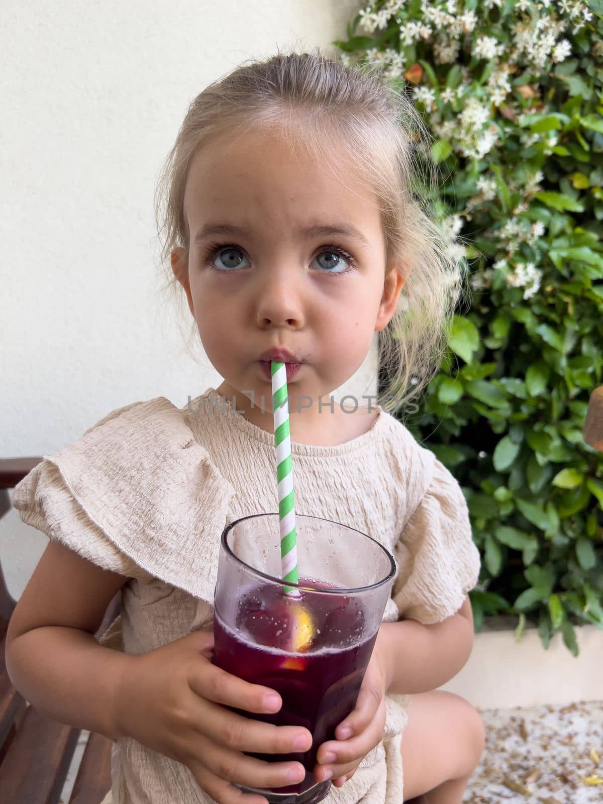 Little girl drinks juice through a straw from a glass holding it in her hands. High quality photo