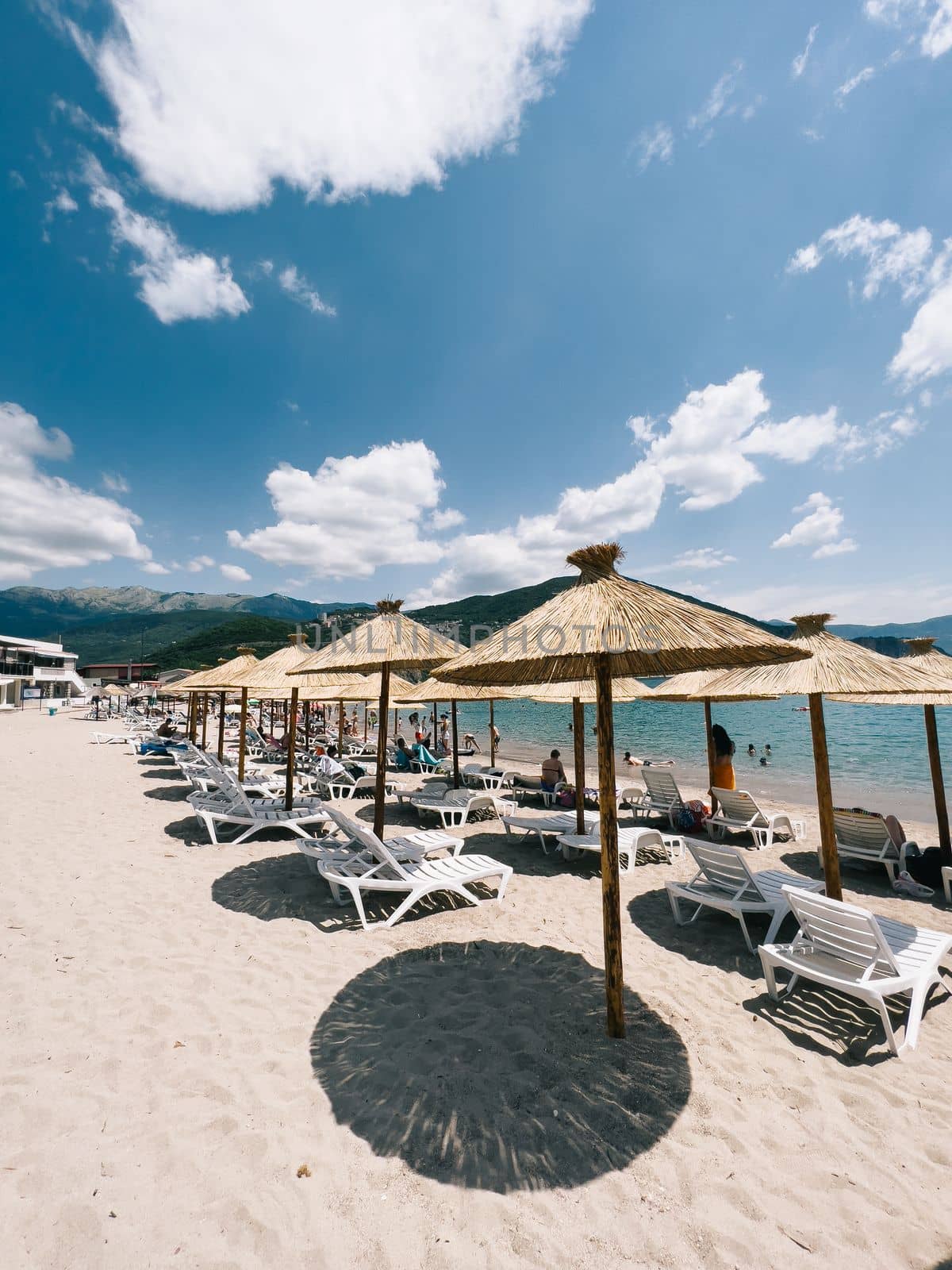 Straw beach umbrellas over sun loungers stand on a sandy beach by the sea. High quality photo