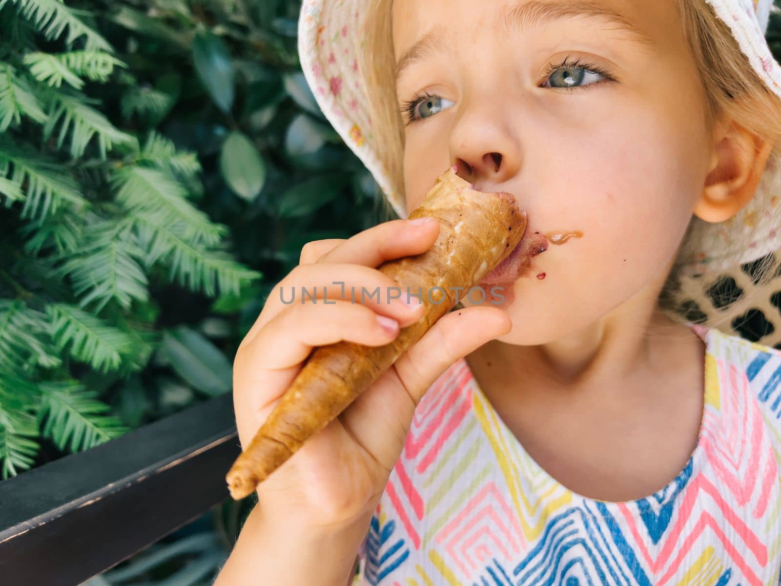 Little girl nibbles on a popsicle in a waffle cone holding it with her hand. High quality photo