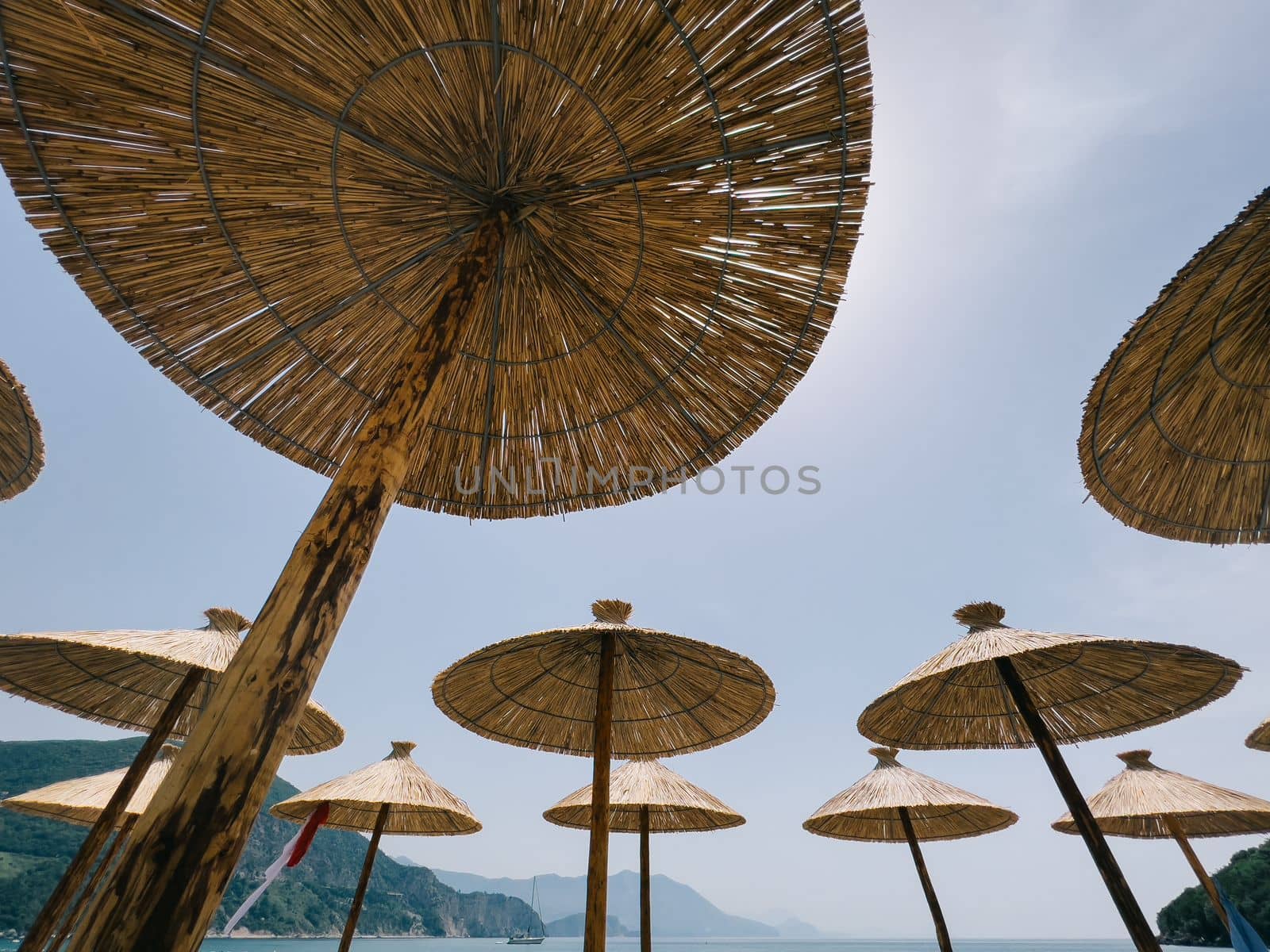 Straw sun umbrellas on the beach by the sea against the backdrop of mountains. High quality photo