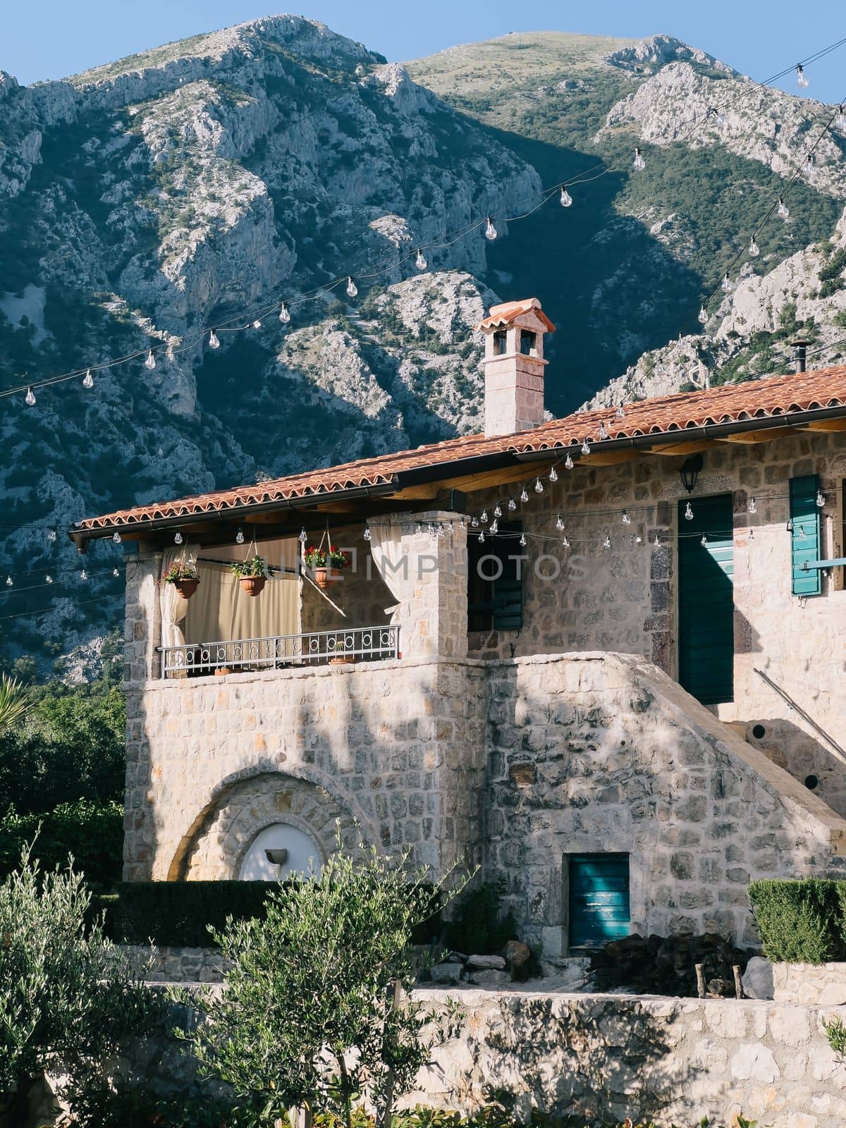 Pots of flowers hang on the terrace of an old stone house at the foot of the mountains. High quality photo