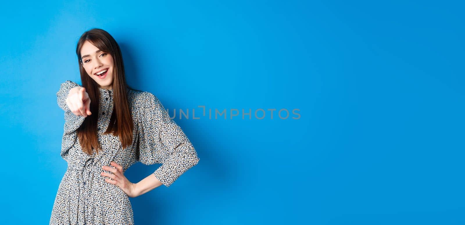 Motivated and excited young woman pointing finger at camera and smiling, congratulating you, praising or inviting, standing happy on blue background.