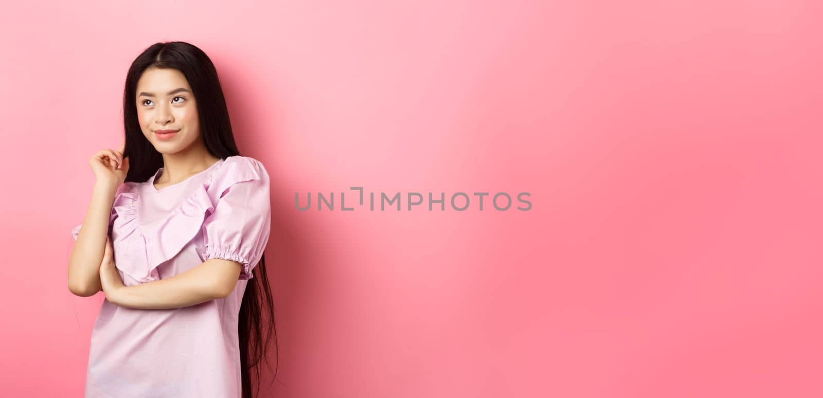 Beautiful asian woman smiling and looking aside, standing in dress on pink romantic background by Benzoix