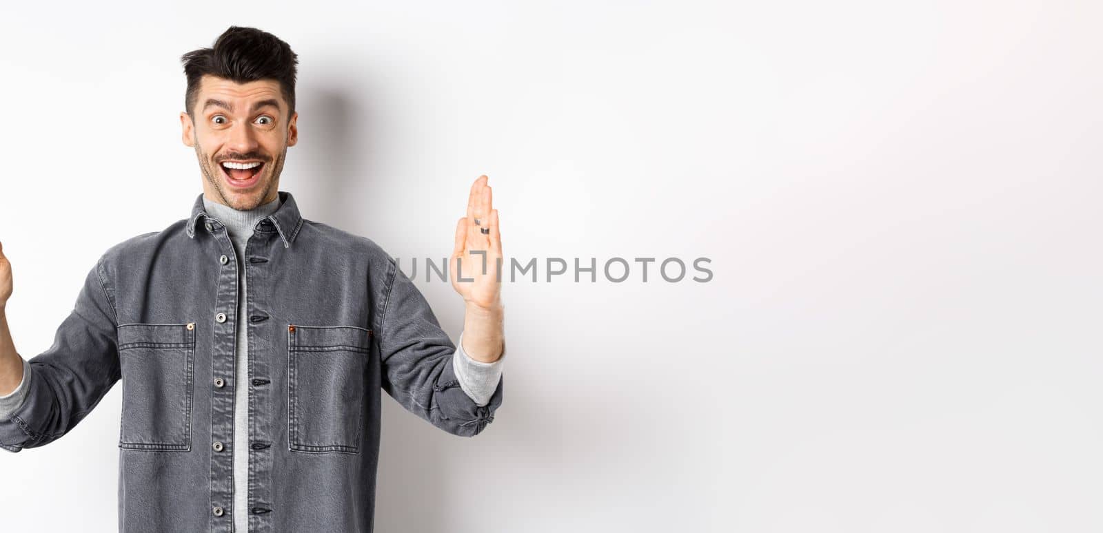 Happy guy with moustache showing big size with proud excited smile, shaping large object, standing in jacket on white background.