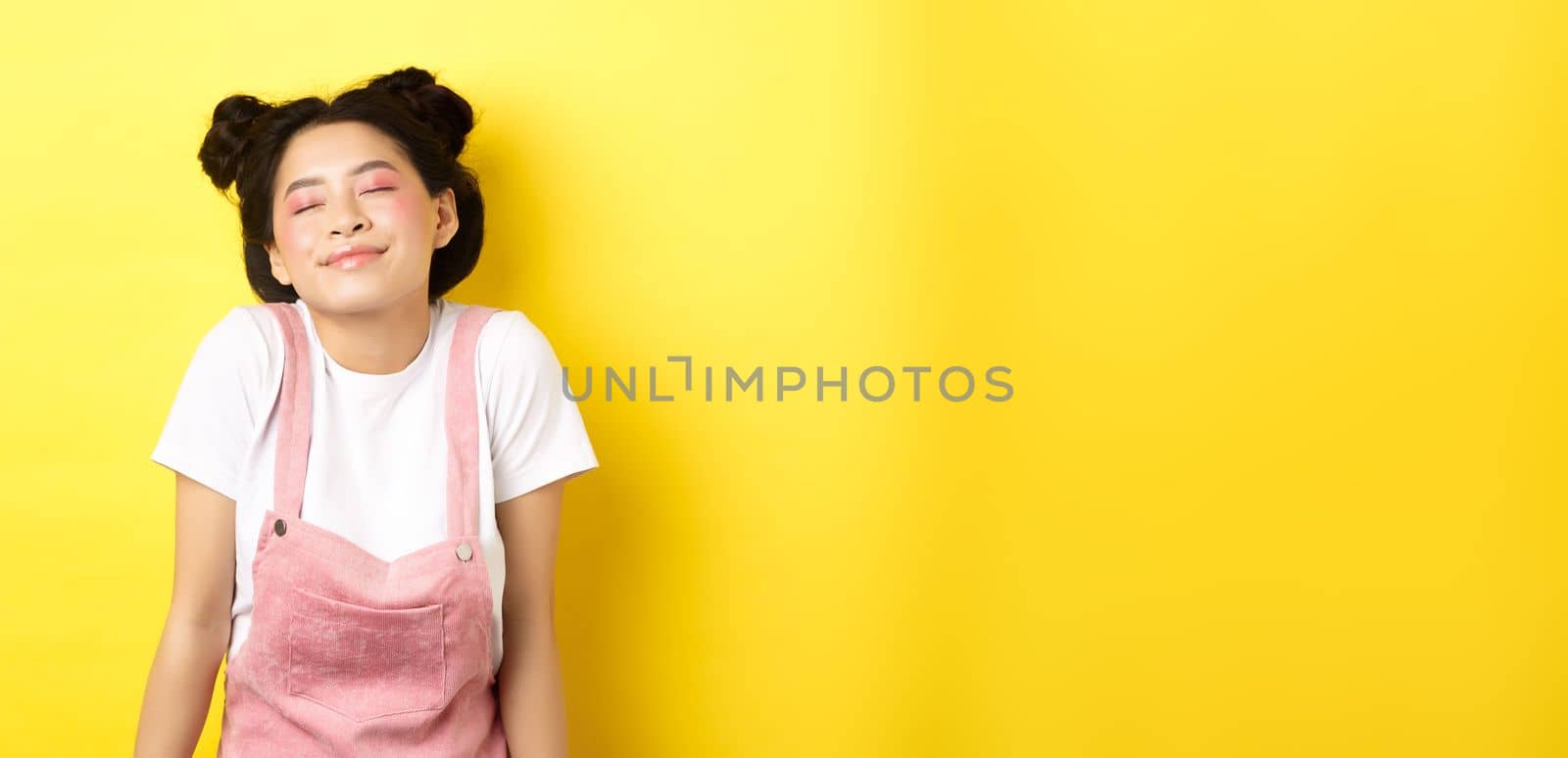 Romantic asian girl with cute pink makeup and summer clothes, close eyes and smiling dreamy, standing on yellow background by Benzoix