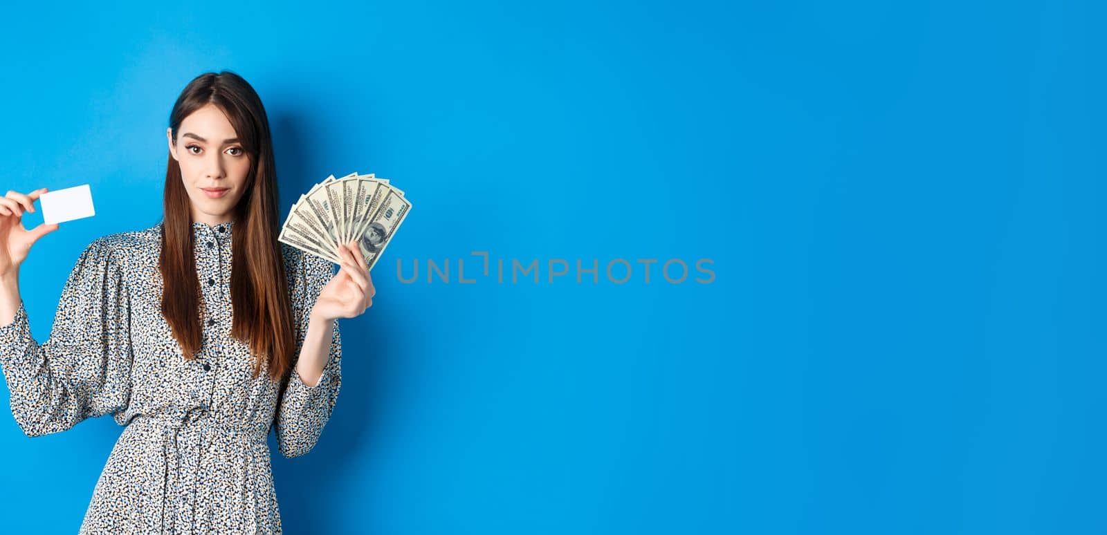 Shopping. Elegant sassy woman with dollar bills money and plastic credit card, looking confident at camera, blue background.