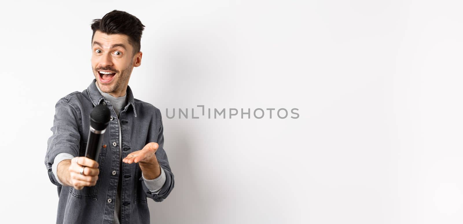 Handsome smiling man stretch out hand with microphone, giving you mic, standing on white background by Benzoix