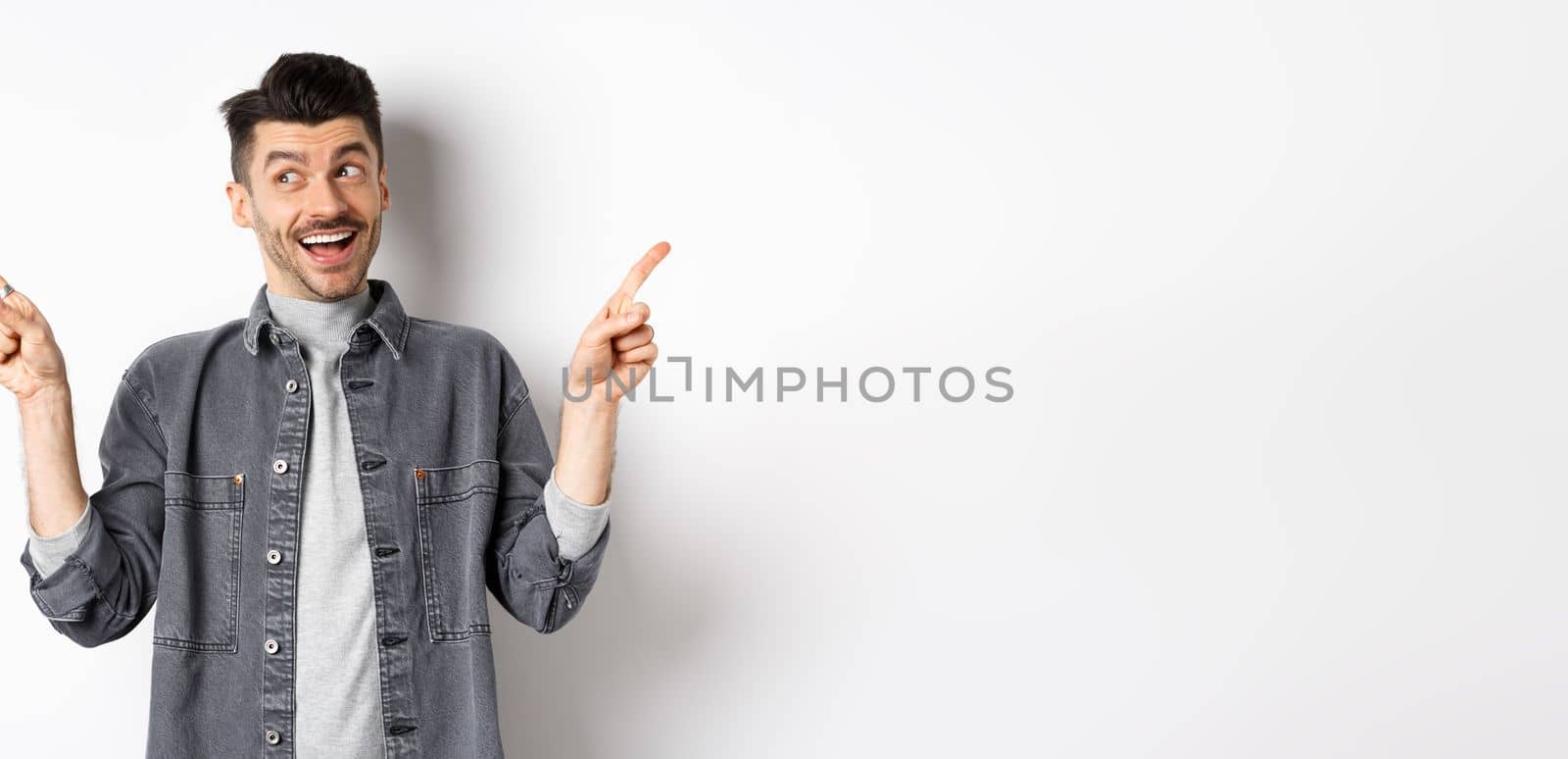 Happy stylish guy laughing and pointing sideways, showing two choices, demonstrate promo offers and smiling, standing against white background.